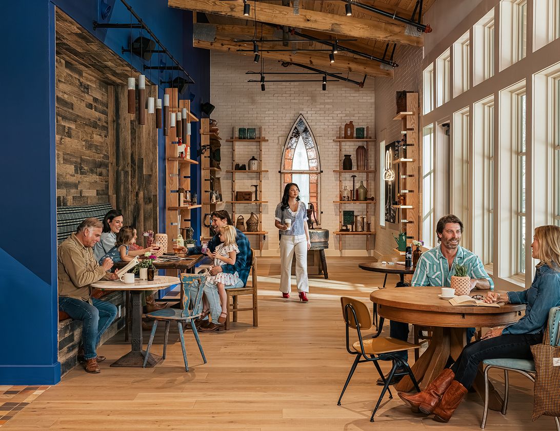 People are sitting and talking in a spacious, modern café with wooden floors, large windows, and contemporary decor at The Grazery restaurant at Two Step Farm.