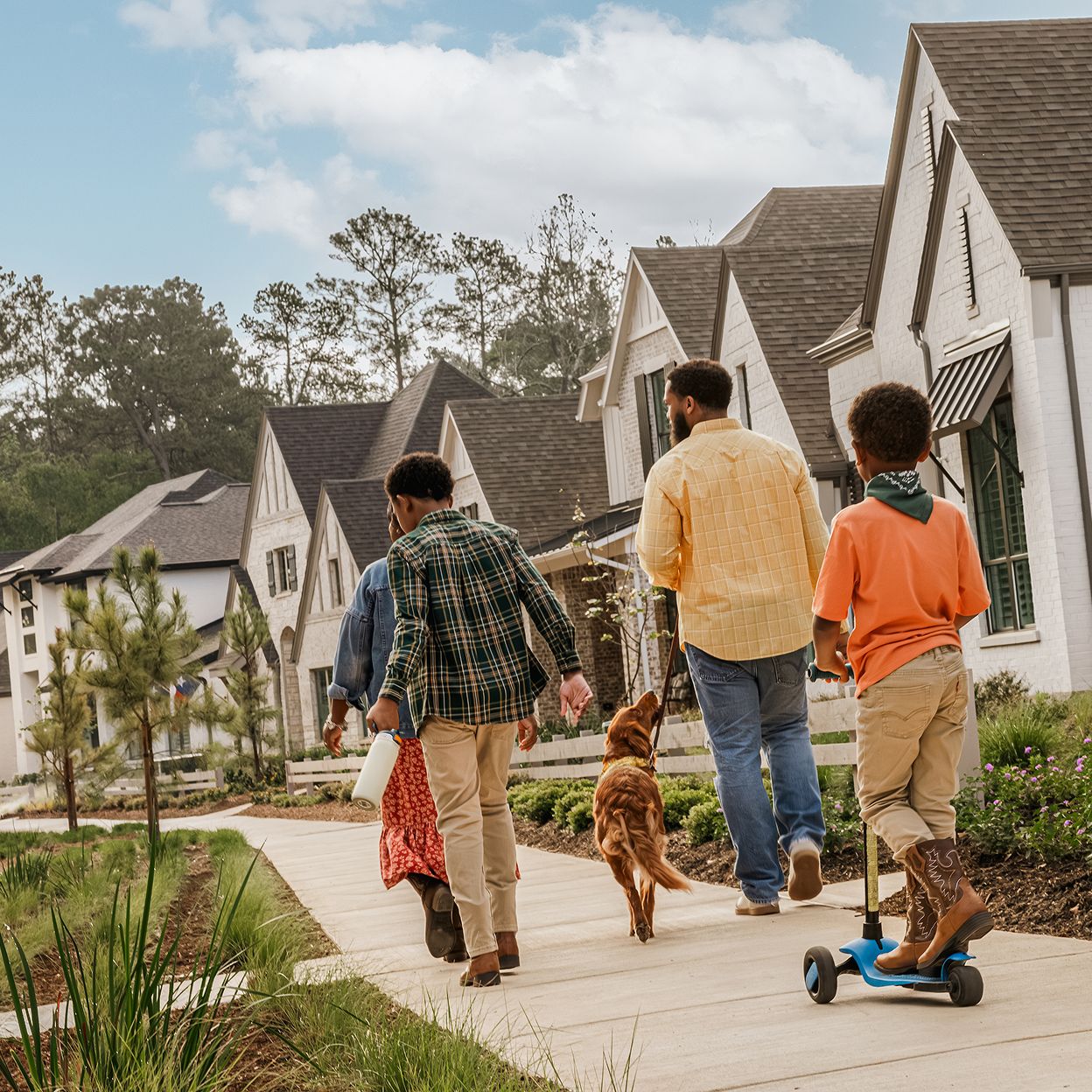 A family with two children and a dog walks along a sidewalk in a suburban neighborhood, enjoying landscaped yards and modern new homes in Montgomery County.
